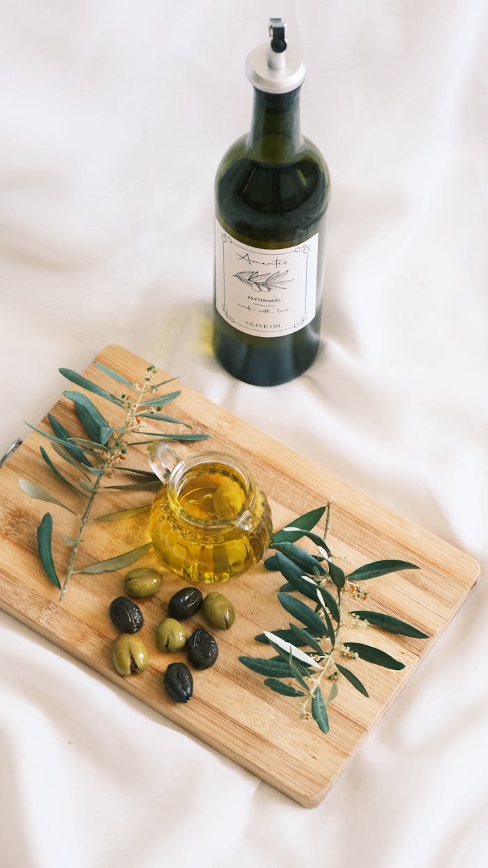 Stylish arrangement of olive oil bottle, olives, and olive branches on a wooden board.